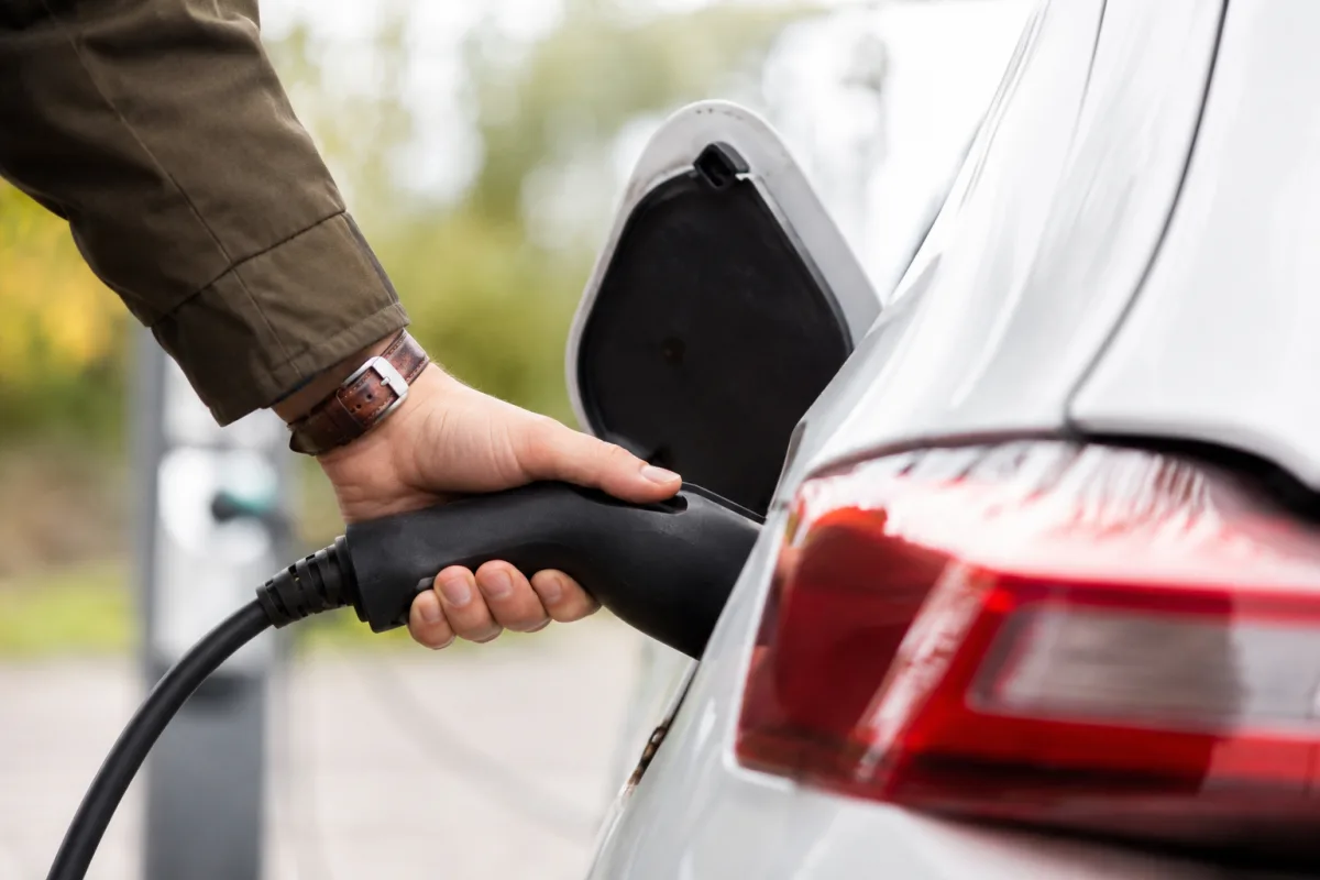Main d'un conducteur branchant un câble de recharge sur la prise d'une voiture électrique blanche